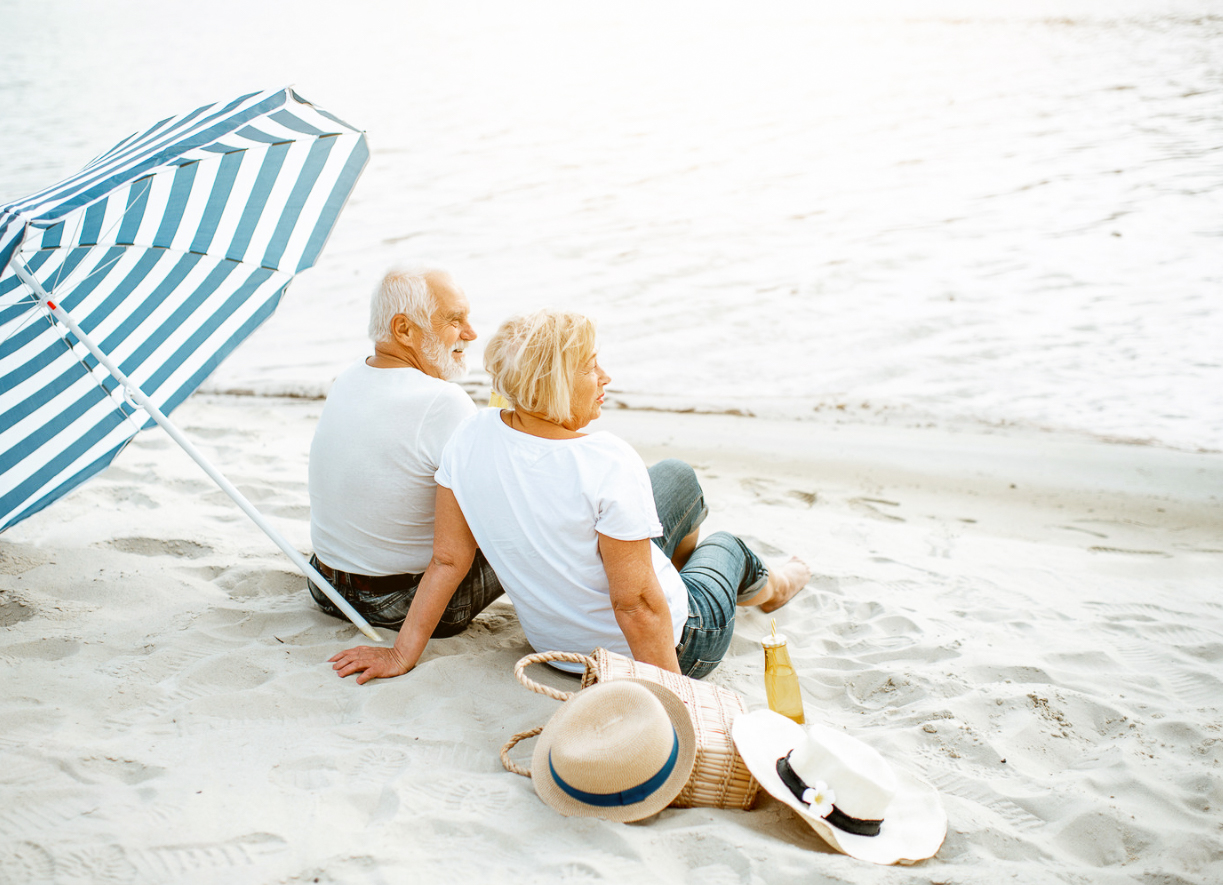 Couple on vacation relaxing on the beach under a blue and white umbrella.