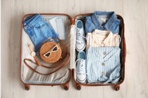 Suitcase packed with a travel capsule wardrobe of blue, white, and yellow travel outfits.