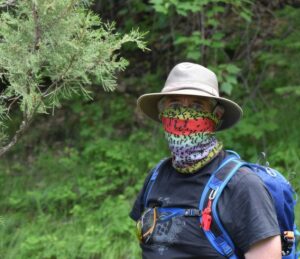 Man out for a hike with backpack, a hat, and a travel bandana tied over his mouth for protection