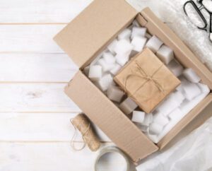 An open box with foam packing peanuts containing a smaller box to check in for travel.