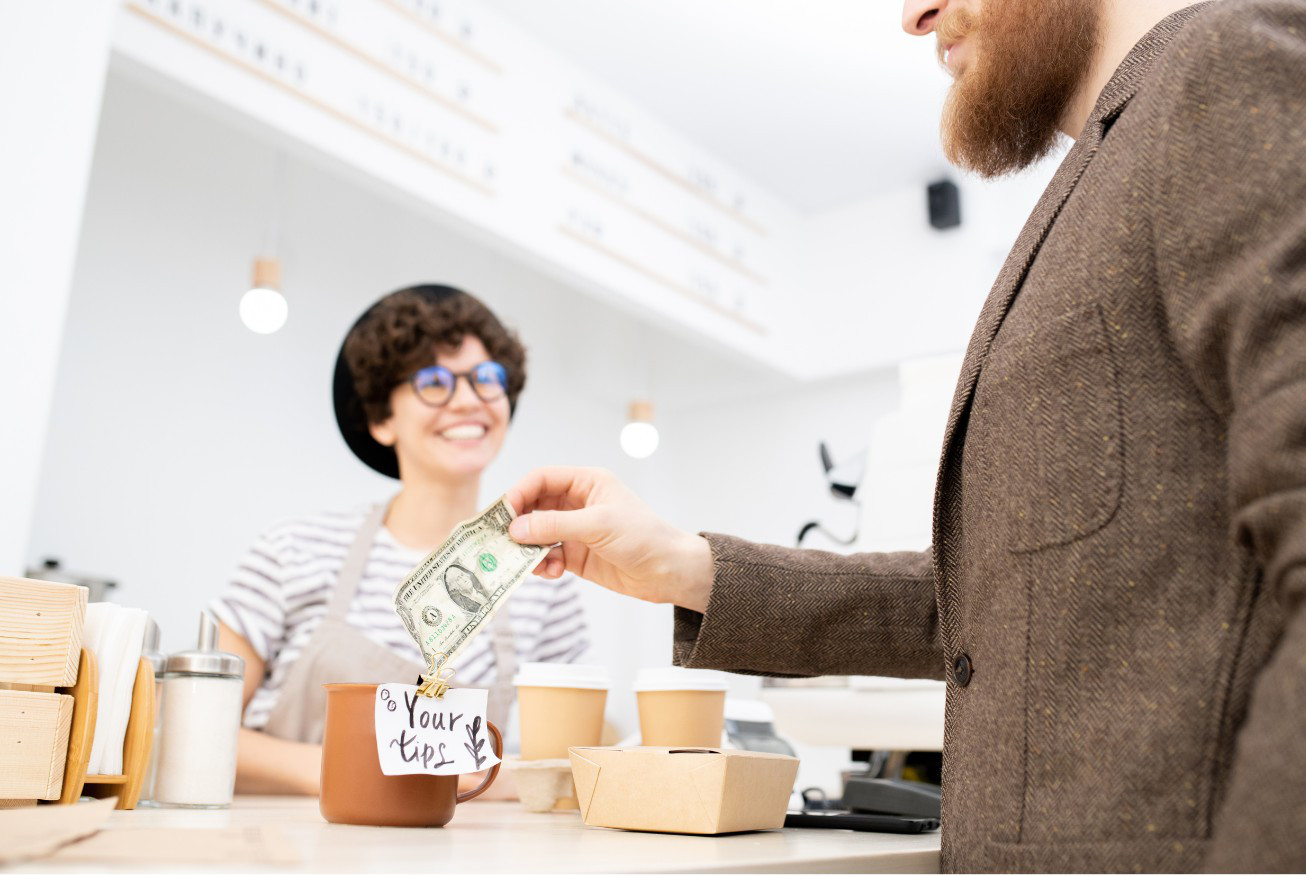 Man putting a dollar into a tip jar at a cafe.