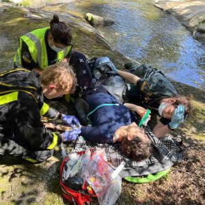 Peggy laying by a river with EMTs attending.